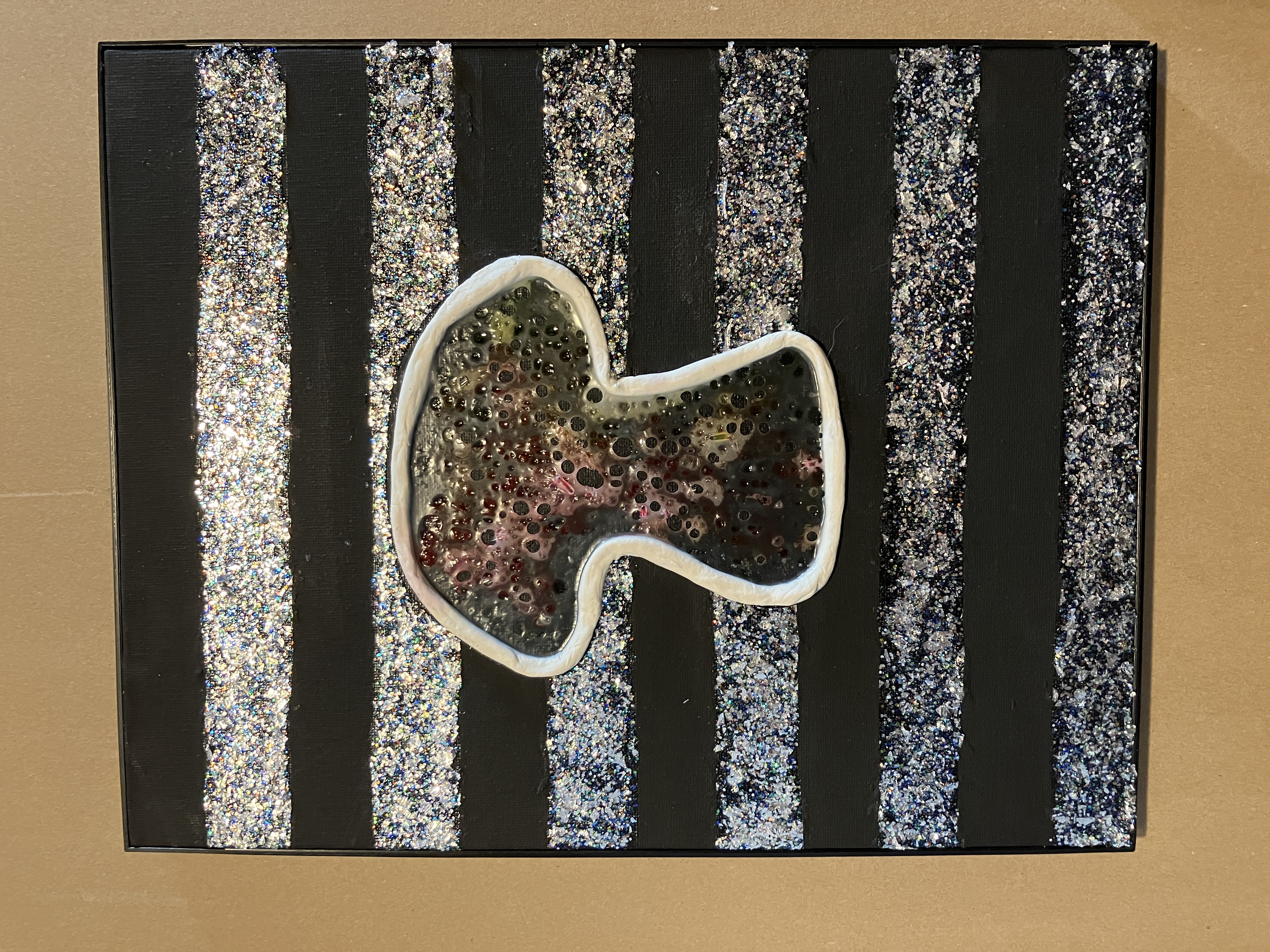 Glue and glow-stick image of mushroom lined in clay on acrylic striped black and silver glitter background